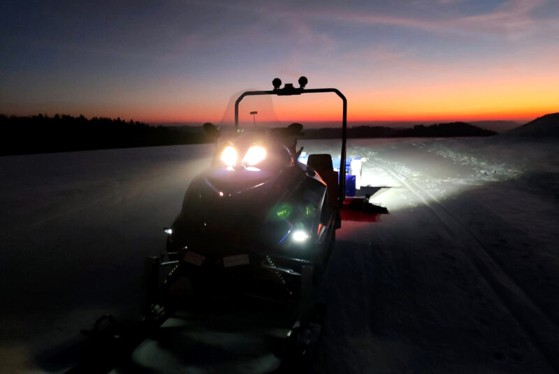 Alpina Superclass dual-track snowmobile grooming a ski trail at sunset